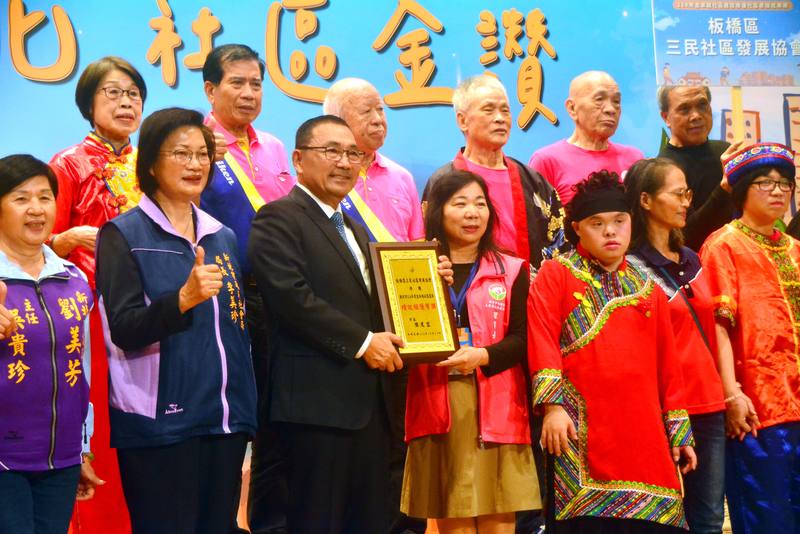 新北市114年度金卓越社區選拔績優社區表揚暨成果展12日登場，會中表揚18個績優社區，榮獲卓越組卓越獎的三芝福成社區開心接受市長侯友宜（前左3）頒獎表揚