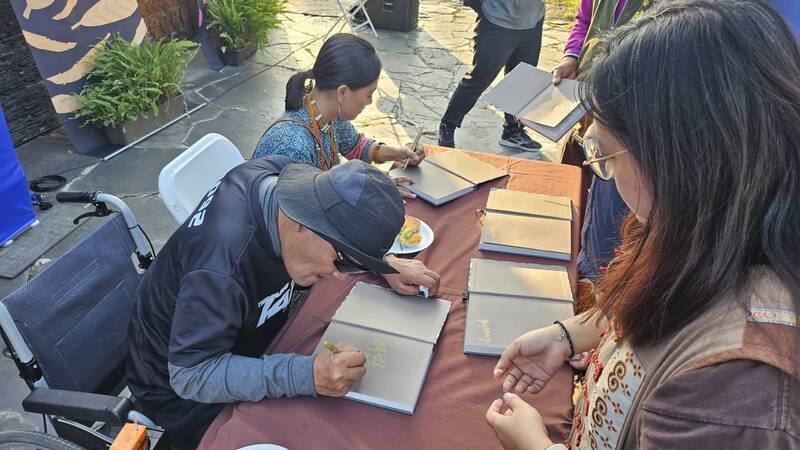 排灣族藝術家秦榮輝（阿瀨）（前左）跨足文學領域，與攝影師張之萓（後左）合著詩集「部落的風」，16日在屏東泰武國小石板屋前正式發表，現場也舉辦簽書會。