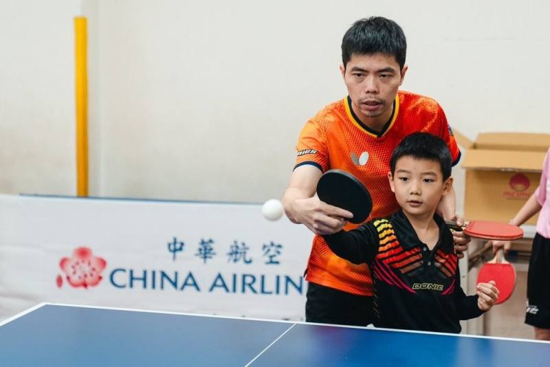 中華航空舉辦公益桌球營，今年移師彰化，並第3度邀請台灣桌球教父莊智淵（後）示範桌球技巧，與學童進行互動教學，包含暖身、握拍、接發球、移動步伐與反應訓練等。（華航提供）