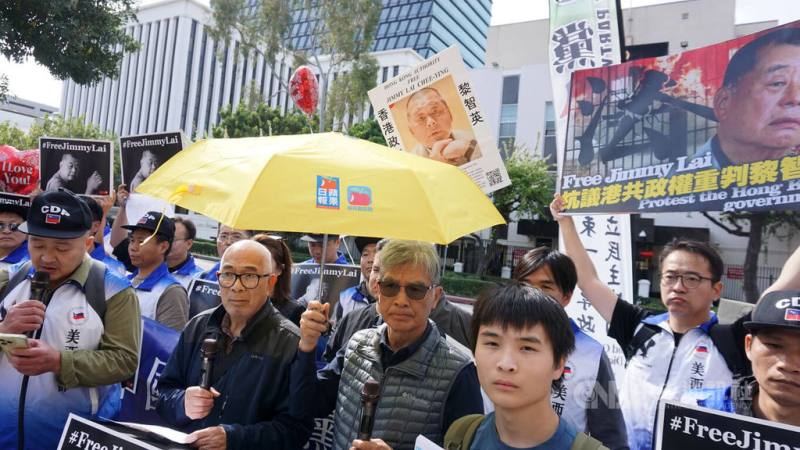 抗議人士聚集在洛杉磯中國領事館前，手舉蘋果日報發送的黃色雨傘，聲援黎智英。前排右1為流亡海外的香港青年梁啟駿