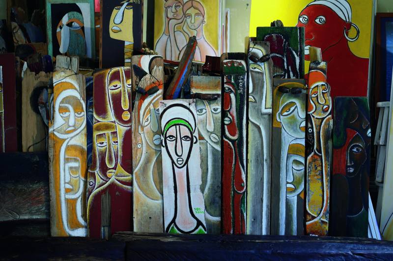 工作室內錯落排列的漂流木畫作，形成一座美麗聚落。畫中人物像在彼此低語交談。