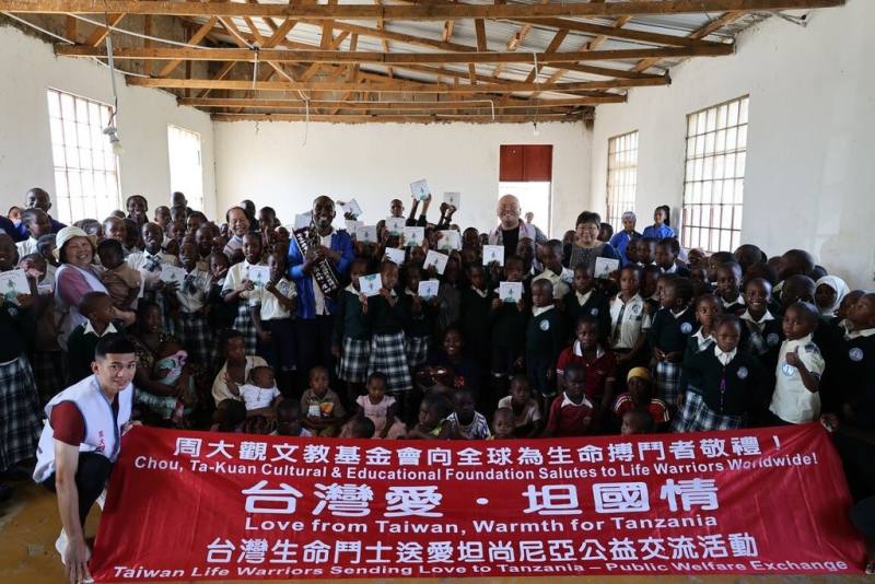周大觀文教基金會創辦人周進華與董事長郭盈蘭率台灣生命鬥士一行，13日在坦尚尼亞穆宛沙Soma Bags社會企業與當地學童合影。當日並與穆宛沙華僑代表王瀋虹合頒「全球熱愛生命獎章」予社會企業創辦人伊諾森特．詹姆士（Innocent James）。（周大觀文教基金會提供）