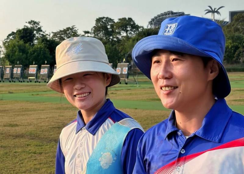 2026年國家運動訓練中心成立50週年，首度推出官方商品，其中漁夫帽讓射箭好手雷千瑩（右）愛不釋手，在練習時直接戴上。（國訓中心提供）
