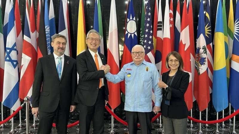 華勒沙前總統（H.E. Lech WAŁĘSA，右二）、華勒沙基金會主席Bogdan WAŁĘSA（左一）、外交部政務次長兼外交學院院長吳志中（左二）及外交學院副院長黎倩儀（右一）於學院大廳國旗前合影。