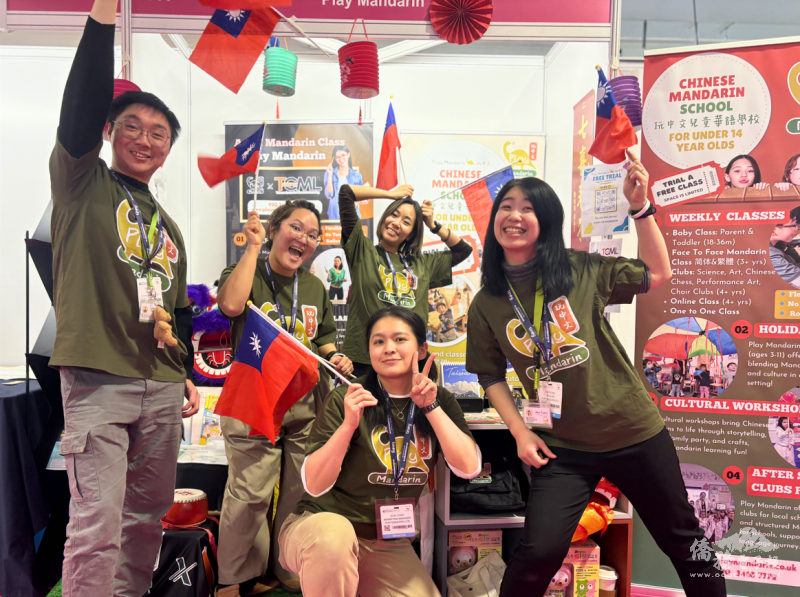 團隊在攤位舉國旗合影，展現充滿活力的教學風采