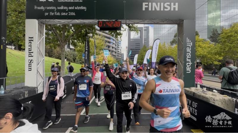臺灣隊高舉旗幟衝破終點線，主播臺同步熱情介紹，現場掌聲與歡呼聲此起彼落，展現團隊士氣與臺灣社群的活力風采