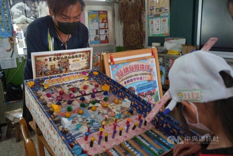 屏東縣東港鎮大潭國小2026年以台語闖關遊戲與手作課程慶祝兒童節，教師夏嘉宏（左）還搬出手作彈珠台與學生同樂。他表示，在陪伴學生透過遊戲學習台語的過程中，自己也回味了童年。