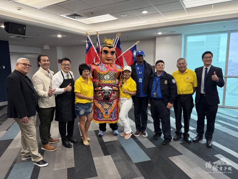 周啟宇(左3)偕僑務秘書杜戎珄(右1)與僑領及TSA人員在餐會會場和三太子合影