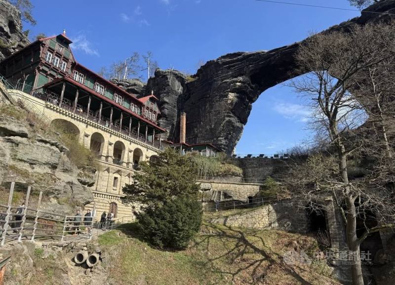 捷克的波希米亞瑞士國家公園（Bohemian Switzerland National Park）有峽谷、岩柱與天然拱門等景觀。這裡有歐洲最壯觀的天然拱岩之一，巨大的灰黑色拱岩橫亙在岩壁上，一旁是紅色與綠色的木造餐廳，形成鮮明對比。