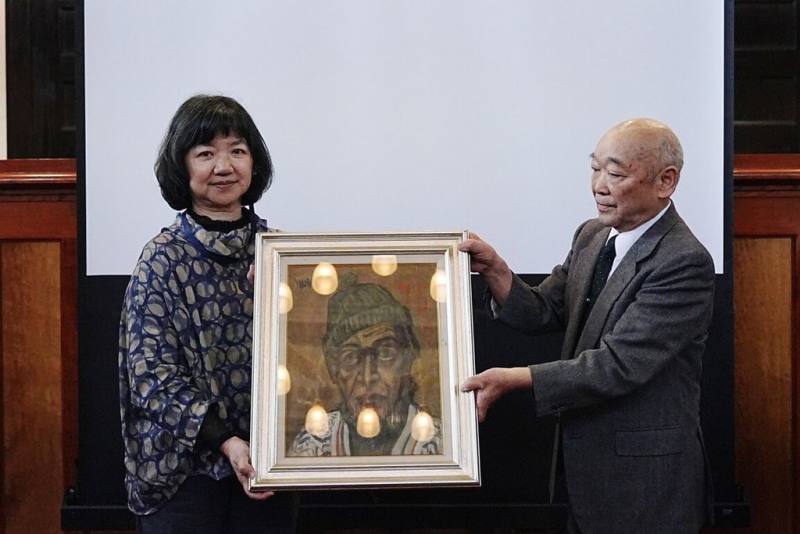 台南國家美術館籌備處25日在日本山口縣台日交流論壇活動，日本藝術家佐伯信夫門生藤崎恒賴（右）特別捐贈佐伯信夫作品「自畫像」給台南國家美術館，由文化部政務次長李靜慧（左）代表受贈。（文化部提供）
