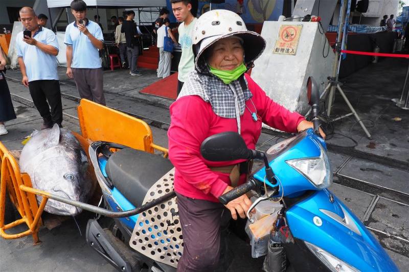 ６．岸邊協助船邊作業的，多半是年長女性。從早年的人力推車，到如今騎著機車載運，圖為今年屏東第一尾進港的黑鮪魚被小心翼翼運送，港邊總能看見這樣充滿生命力的風景。
Most of those assisting with dockside operations are older women. From handcarts in the early days to motor scooters today, transport methods have evolved. Pictured here is t