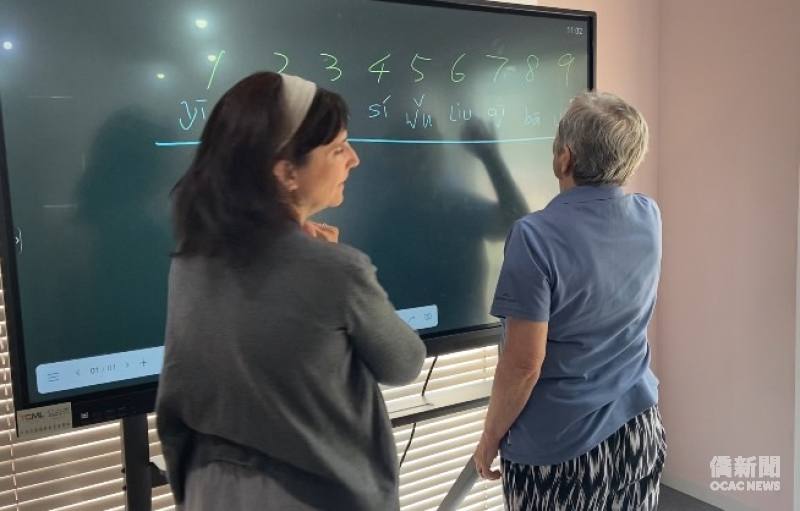 Ruth (right) writes the tone marks for numbers on the board while practising Mandarin tones.