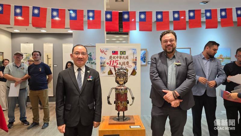 尤正才（左）、Thiago Delmonde Ribeiro(右)在國慶海報及三太子雕塑前合影。