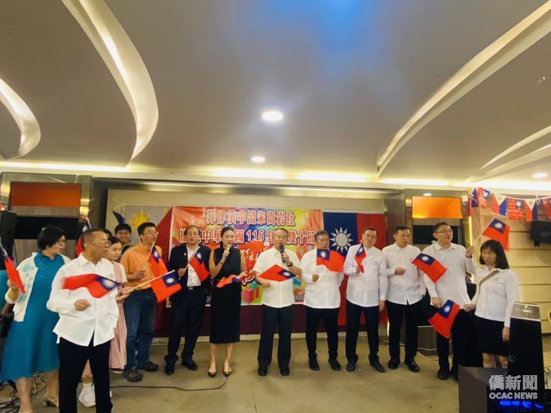 周民淦與中呂宋僑界代表揮舞中華民國國旗，齊聲高唱〈梅花〉及〈中華民國頌〉，展現海外僑胞團結一心的精神與愛國情懷。