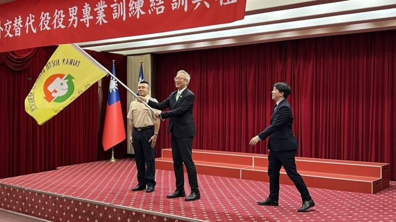 國合會21日舉辦「第26屆外交替代役專業訓練結訓典禮」，由外交部政務次長吳志中（中）主持，並為此屆外交替代役授旗。（國合會提供）