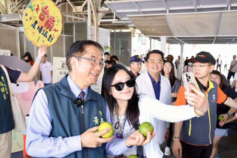 台南火車站舊軌道開放活動吸引民眾湧入拍照體驗，市長黃偉哲（前左）26日帶著台南特產東山椪柑前往與遊客分享。（台南市政府提供）